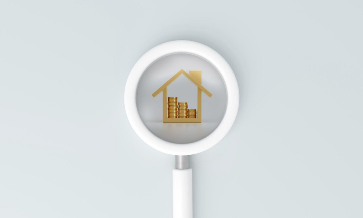 Image illustrant le concept d'estimation de la valeur d'un bien immobilier représenté par une loupe posée sur une maison ayant des pièces en son intérieur.
